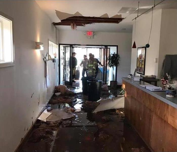 Hole on ceiling, ceiling tiles on floor, standing water on floor, firefighters on entrance door