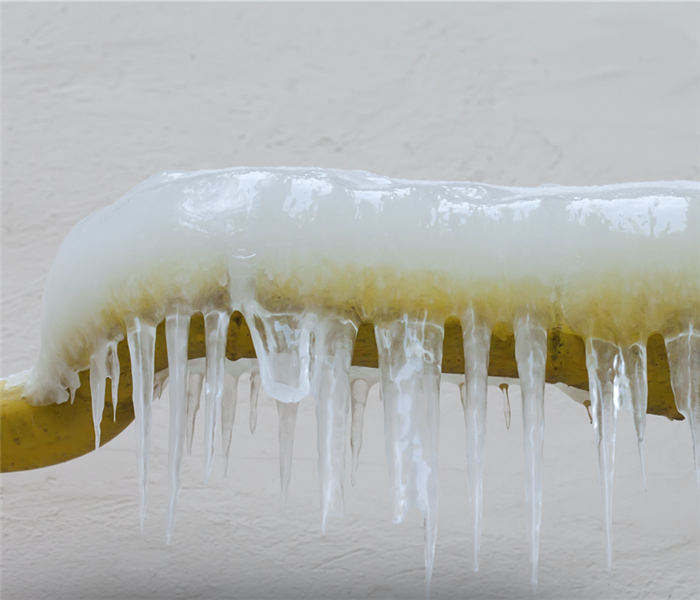 Icicles hanging from a frozen water jets, tube, yellow pipe. aged wall background. winter time concept 