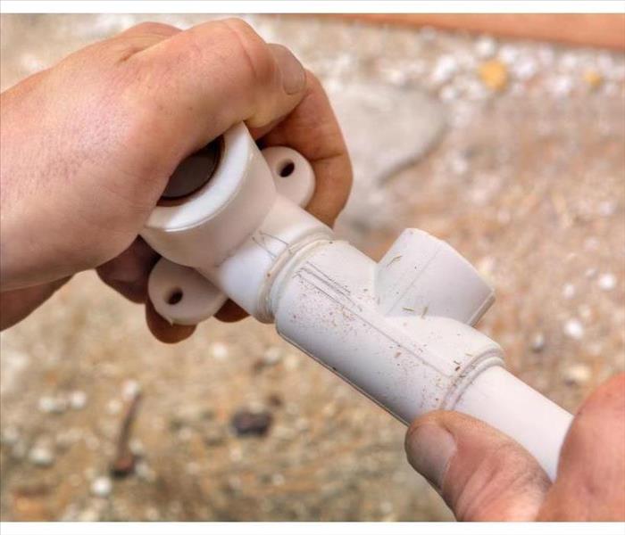 The plumber connects parts of the plastic water pipe using fittings, hands close-up.